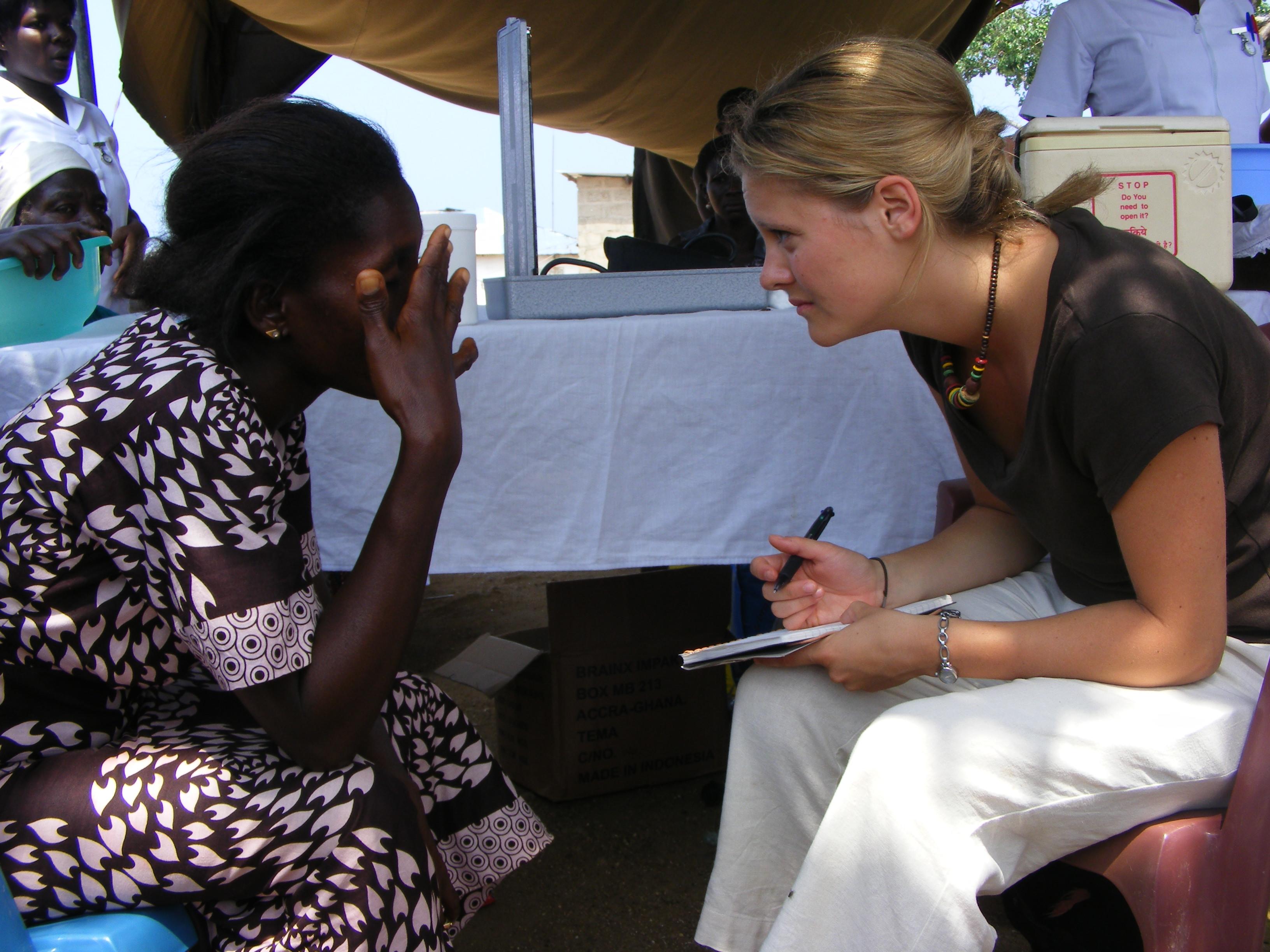 Projects Abroad Medical intern sits down with a local woman during an International medical internship in Ghana. Female medical intern sits across a woman with a pad during Community Outreach programme in Ghana.